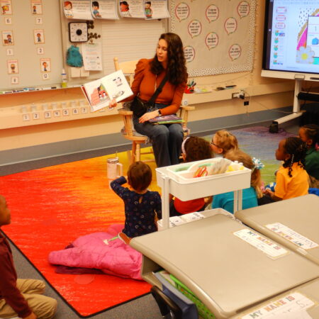 a person sitting in a chair reading a book to children