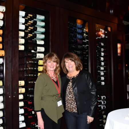 a couple of women standing in front of a wine rack