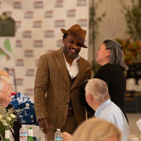 a person in a brown suit and hat standing in front of a group of people
