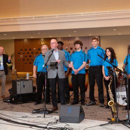 a person standing in front of a microphone with a group of people in the background