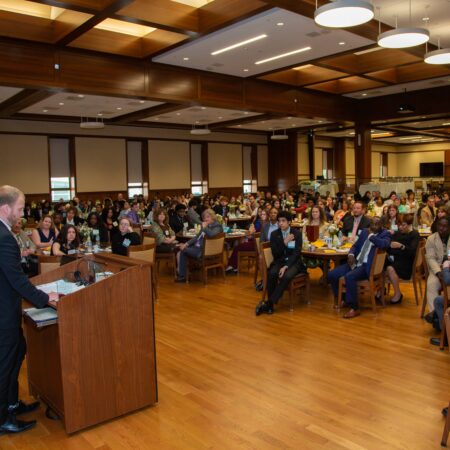 a person standing at a podium in front of a group of people seated in a room
