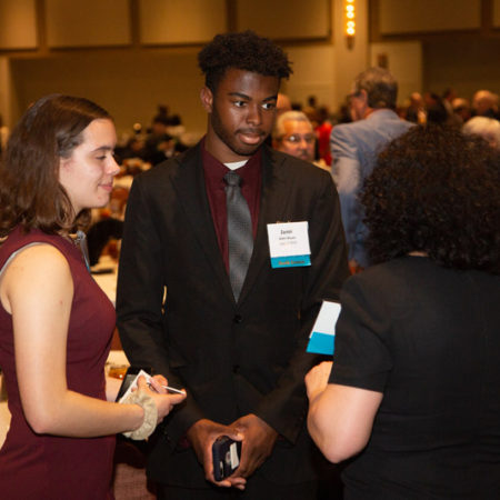 a person in a suit and tie standing in a room with people