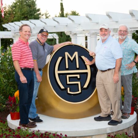 a group of men standing next to a large gold and black sign