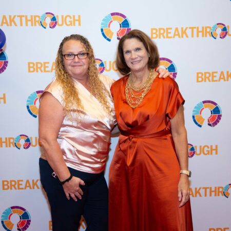 two women standing together in front of a wall with text