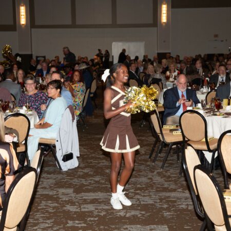 a cheerleader holding flowers in a room with people seated in the background