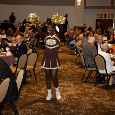 a cheerleader waving in a room with people sitting around