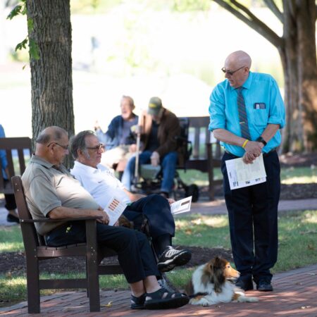 a person standing next to a group of men sitting on a bench