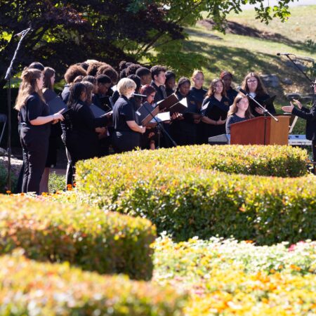 a group of people singing in front of bushes