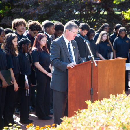 a person standing at a podium with a crowd of people behind him