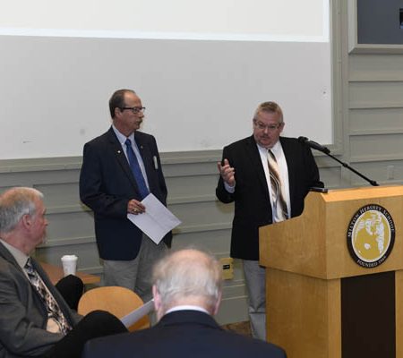 a person standing at a podium with a person holding papers
