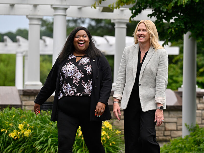Trachanda García and Mary Pratt-Lauchle walking in the Friendship Garden on the grounds of the Dearden Alumni Campus.